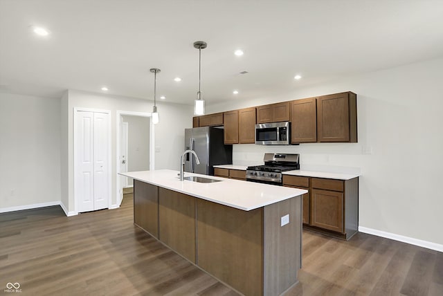 kitchen featuring appliances with stainless steel finishes, a kitchen island with sink, dark wood-type flooring, pendant lighting, and sink