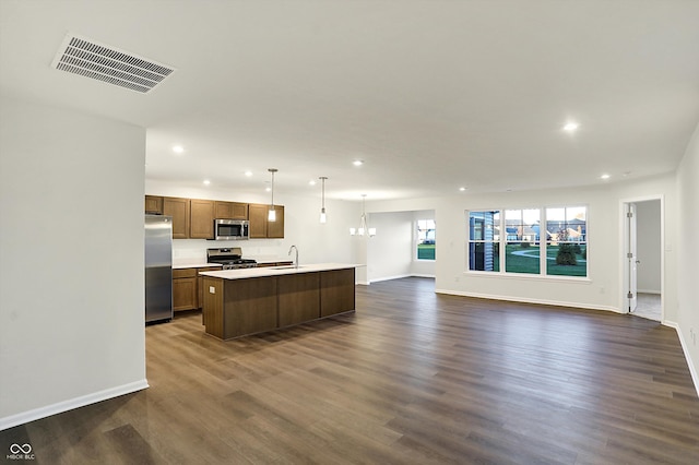 kitchen with dark hardwood / wood-style flooring, appliances with stainless steel finishes, a kitchen island with sink, pendant lighting, and sink