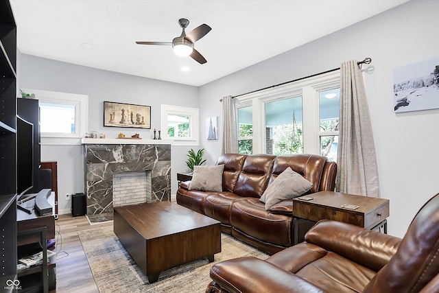 living room with a stone fireplace, ceiling fan, and light hardwood / wood-style floors