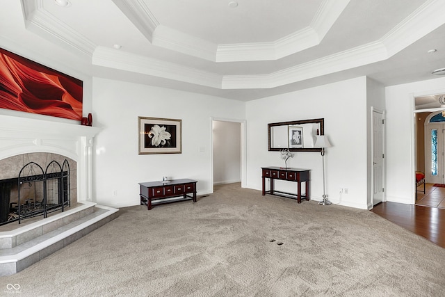 living room featuring carpet floors, a tray ceiling, crown molding, a tile fireplace, and baseboards