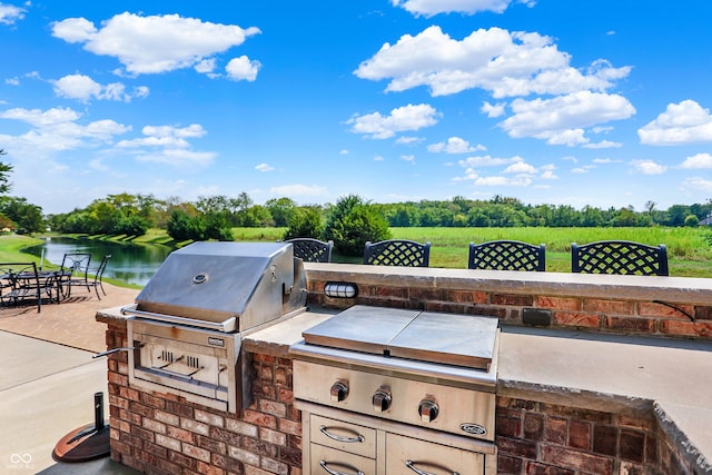 view of patio featuring exterior kitchen, a water view, and a grill