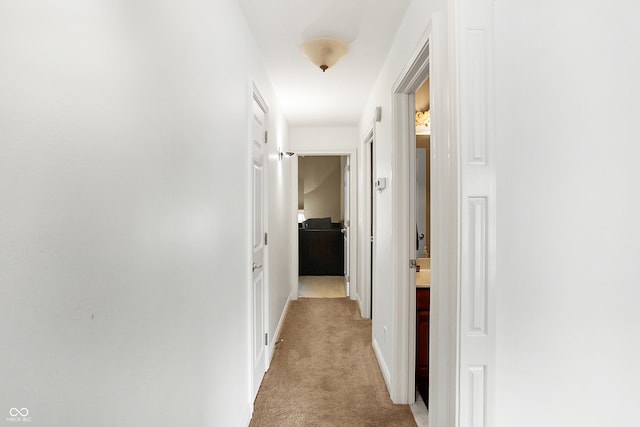 hallway with baseboards and light colored carpet