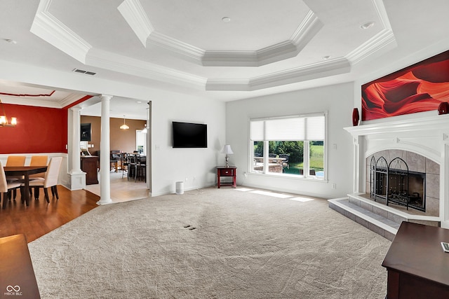 living room featuring a fireplace, a notable chandelier, a tray ceiling, wood-type flooring, and ornamental molding