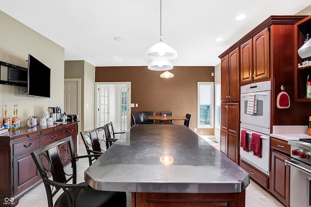 kitchen featuring high end stainless steel range oven, pendant lighting, light tile patterned floors, a center island, and double oven