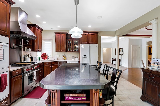 kitchen with a kitchen island, white appliances, wall chimney exhaust hood, decorative columns, and light wood-type flooring