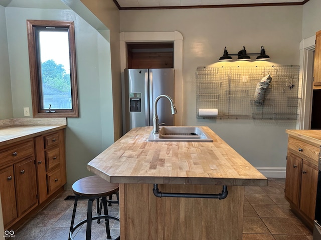 kitchen featuring butcher block countertops, an island with sink, sink, a breakfast bar, and stainless steel fridge with ice dispenser