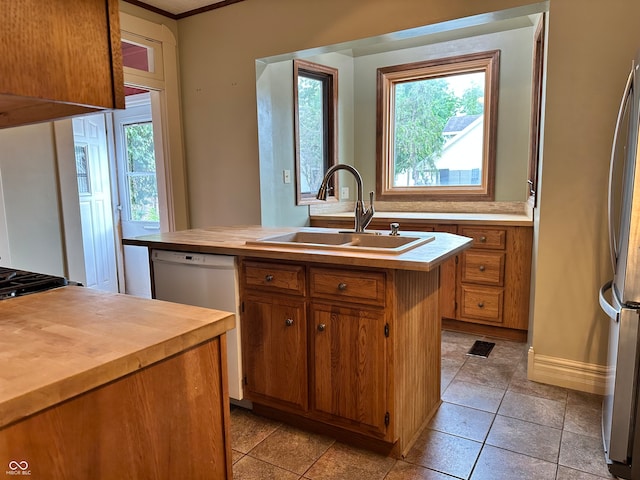 kitchen with a kitchen island with sink, stainless steel refrigerator, dishwasher, sink, and light tile patterned flooring