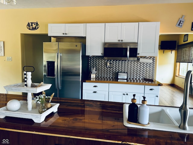 kitchen with hardwood / wood-style floors, stainless steel appliances, decorative backsplash, and white cabinetry