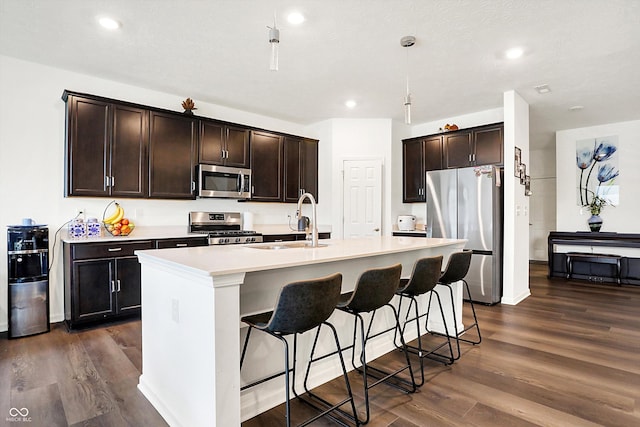 kitchen with stainless steel appliances, dark hardwood / wood-style flooring, sink, a breakfast bar, and a center island with sink