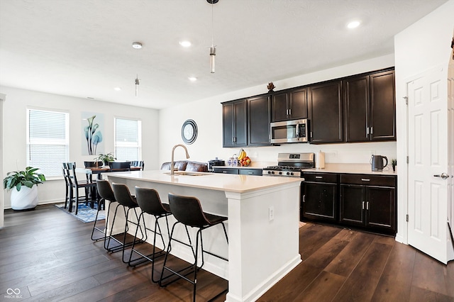 kitchen with stainless steel appliances, sink, dark hardwood / wood-style flooring, and a kitchen island with sink