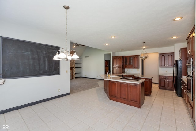 kitchen with decorative light fixtures, a center island with sink, light countertops, black appliances, and baseboards