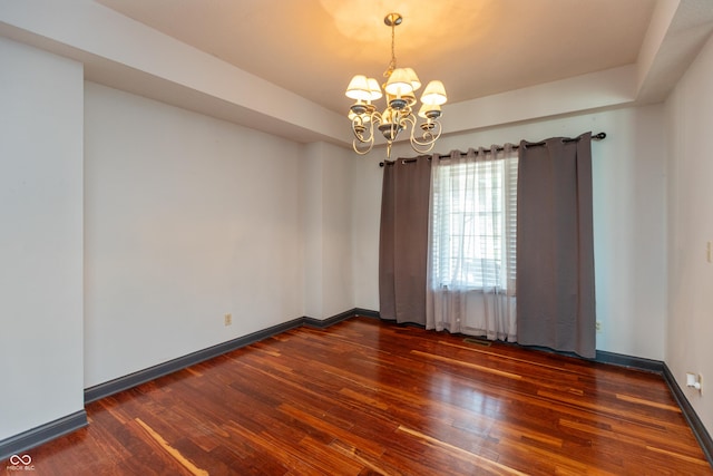 spare room featuring a notable chandelier, baseboards, a raised ceiling, and wood finished floors