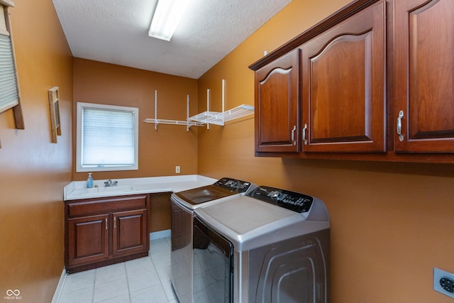 laundry area with light tile patterned floors, a textured ceiling, washing machine and dryer, a sink, and cabinet space