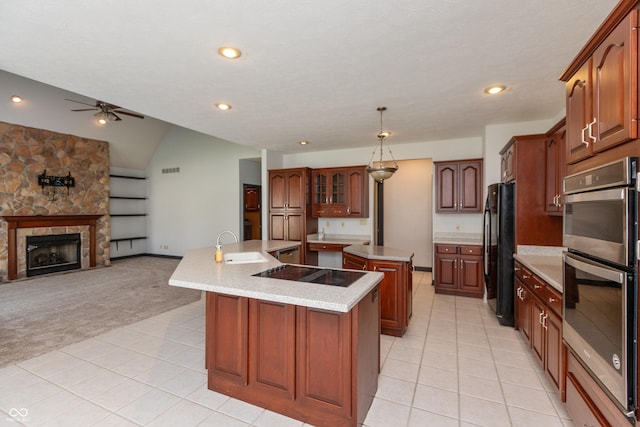 kitchen with a fireplace, a center island with sink, light colored carpet, a sink, and black appliances