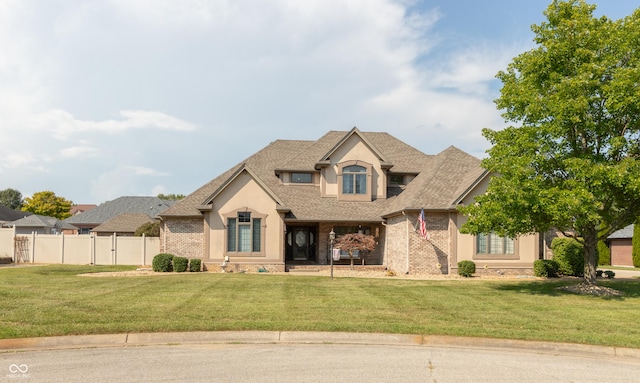 view of front facade featuring a front lawn, fence, brick siding, and stucco siding