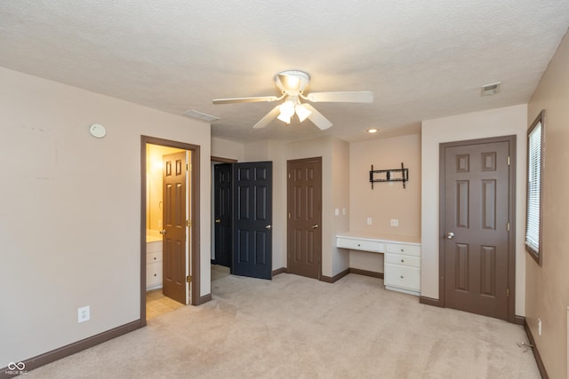 unfurnished bedroom featuring a textured ceiling, light colored carpet, visible vents, baseboards, and built in study area