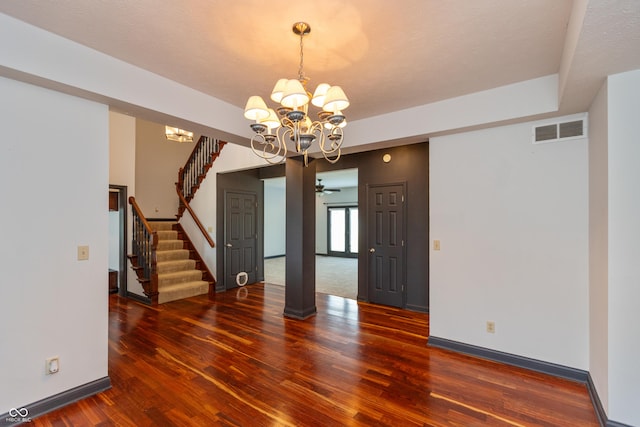 empty room with a notable chandelier, visible vents, stairway, wood finished floors, and baseboards