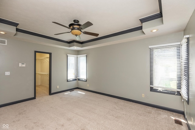 spare room with light carpet, baseboards, visible vents, a raised ceiling, and ornamental molding