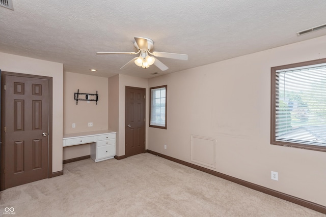 unfurnished bedroom with light carpet, a textured ceiling, baseboards, and built in desk