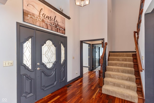 foyer entrance featuring dark wood-style floors, visible vents, stairway, a high ceiling, and baseboards