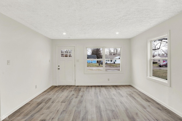 entryway with a wealth of natural light, a textured ceiling, and light hardwood / wood-style flooring