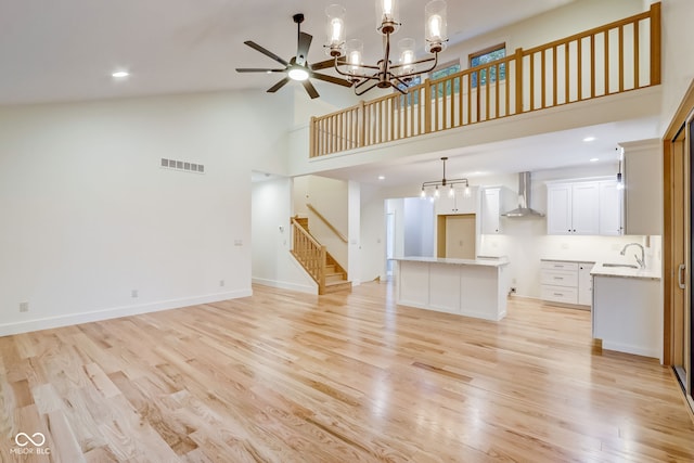 unfurnished living room with high vaulted ceiling, stairway, ceiling fan with notable chandelier, light wood-type flooring, and visible vents