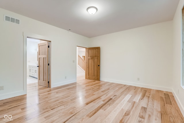 unfurnished room with baseboards, light wood-style flooring, visible vents, and stairs