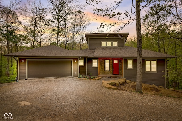 view of front facade with a shingled roof, dirt driveway, and a garage