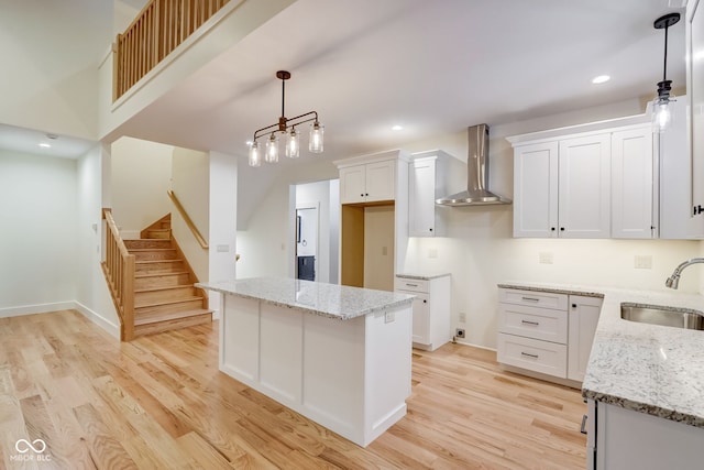 kitchen with a sink, light wood-style floors, white cabinetry, wall chimney range hood, and a kitchen island