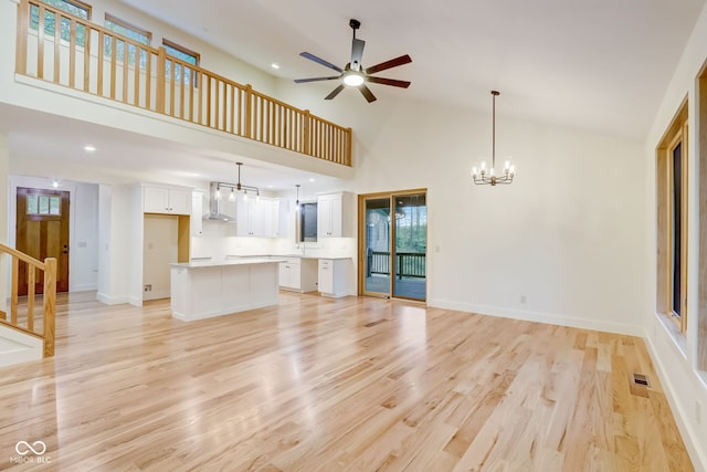 unfurnished living room featuring light wood finished floors, baseboards, visible vents, ceiling fan with notable chandelier, and high vaulted ceiling