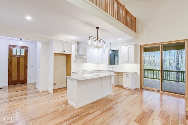 kitchen with a kitchen island, light wood-type flooring, wall chimney exhaust hood, and white cabinets