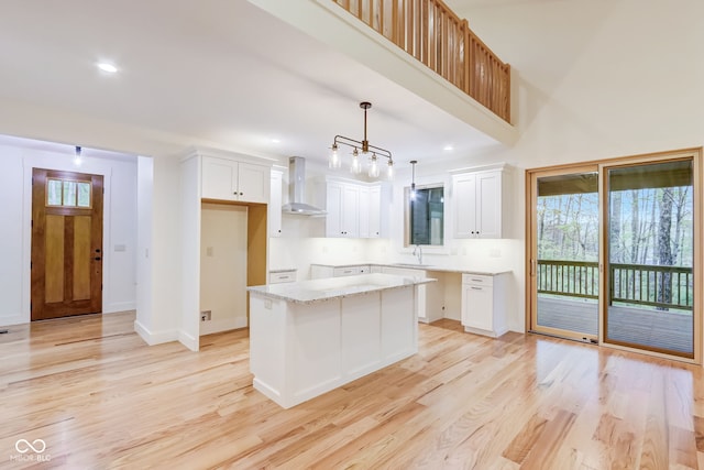 kitchen featuring wall chimney range hood, a sink, light wood-style floors, a kitchen island, and white cabinetry