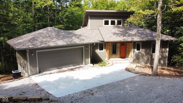 prairie-style home with cooling unit, an attached garage, a shingled roof, and concrete driveway