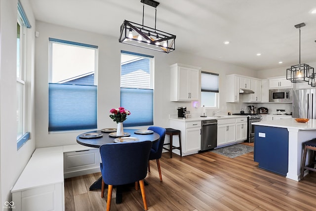 kitchen featuring light wood-type flooring, hanging light fixtures, white cabinets, appliances with stainless steel finishes, and a center island