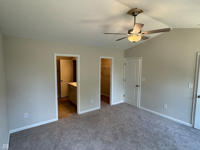 unfurnished bedroom with ceiling fan, connected bathroom, a walk in closet, a closet, and vaulted ceiling