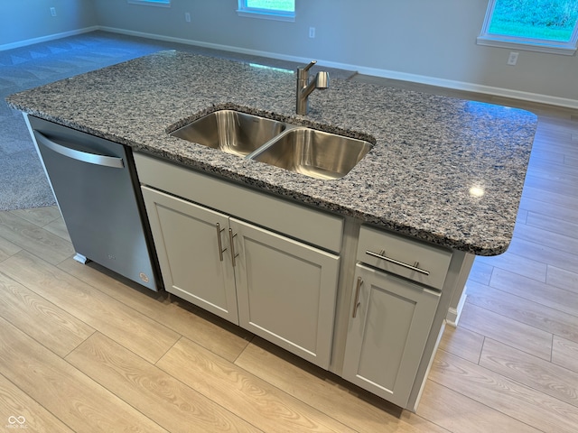 kitchen with light hardwood / wood-style floors, dark stone counters, dishwasher, a center island with sink, and sink