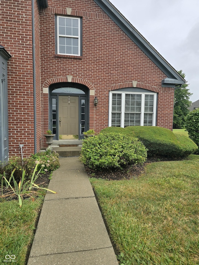 property entrance with brick siding and a lawn