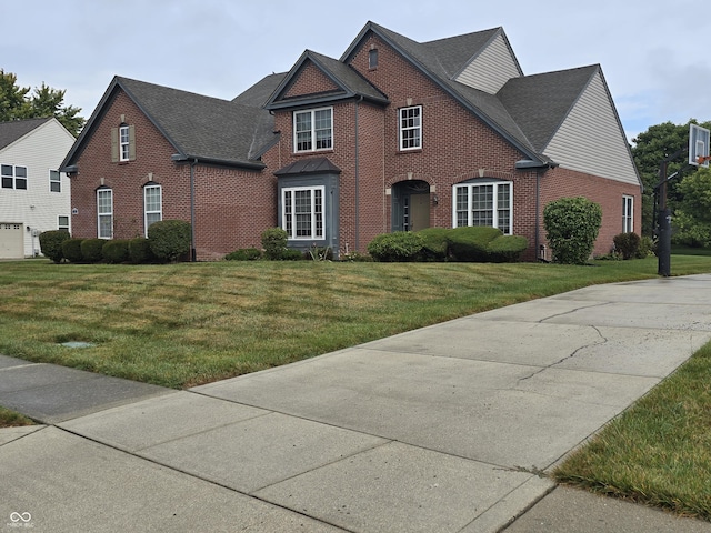 view of front of house with a shingled roof, a front lawn, and brick siding