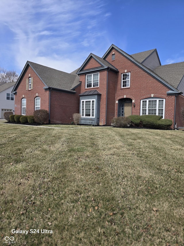 traditional-style home with a front yard, brick siding, and a shingled roof