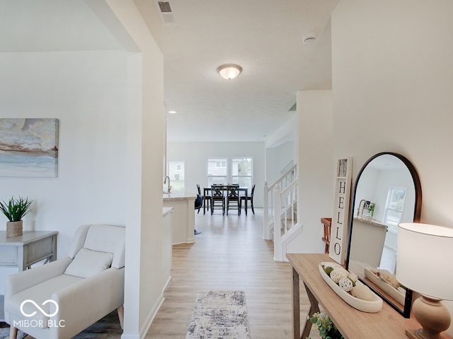 corridor featuring visible vents, light wood-style floors, a sink, baseboards, and stairs