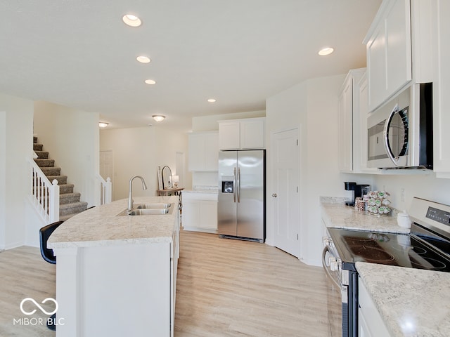 kitchen with appliances with stainless steel finishes, light wood-style floors, white cabinets, and a sink