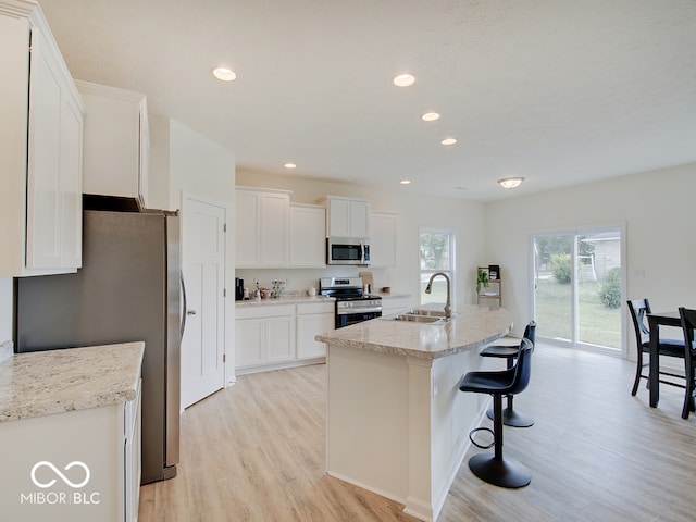 kitchen with a breakfast bar area, a sink, white cabinetry, appliances with stainless steel finishes, and light wood-type flooring