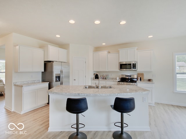 kitchen with appliances with stainless steel finishes, light wood-type flooring, a sink, and a kitchen breakfast bar