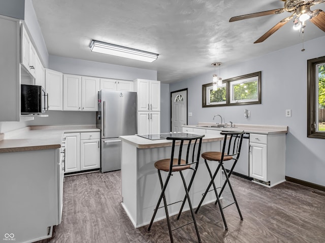 kitchen featuring a breakfast bar area, stainless steel appliances, white cabinets, a center island, and dark wood finished floors