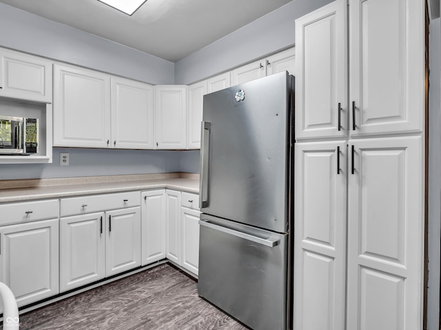 kitchen with light countertops, freestanding refrigerator, white cabinetry, and wood finished floors