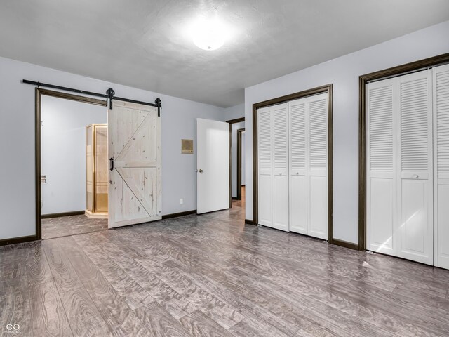 unfurnished bedroom featuring multiple closets, hardwood / wood-style flooring, connected bathroom, and a barn door