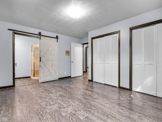 unfurnished bedroom featuring two closets, a barn door, baseboards, and wood finished floors