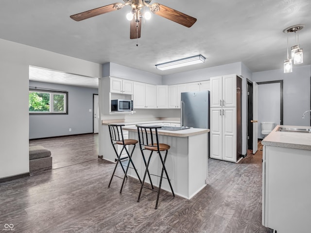 kitchen featuring a breakfast bar area, stainless steel appliances, white cabinets, a sink, and wood finished floors