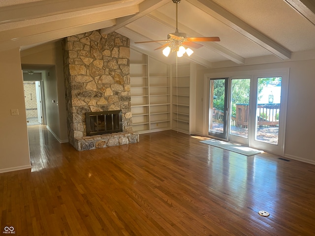 unfurnished living room featuring a stone fireplace, built in features, dark wood-type flooring, ceiling fan, and vaulted ceiling with beams