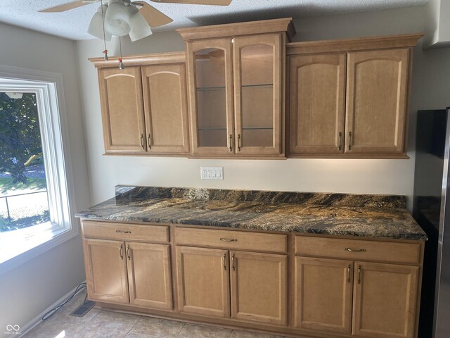 kitchen with dark stone countertops, stainless steel fridge, a textured ceiling, ceiling fan, and light tile patterned flooring